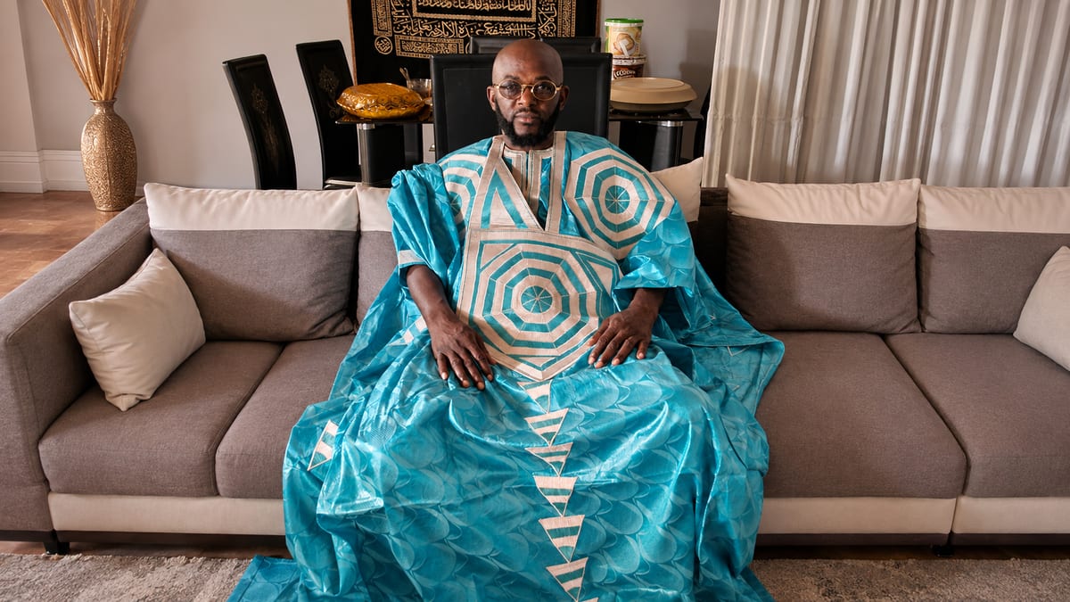 Marabout Djibril de túnica turquesa, sentado na sua sala